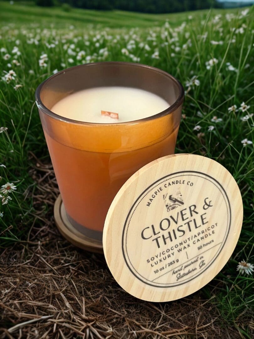 Candle jar in grass with wooden lid.