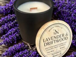Black candle on lavender with lid nearby.