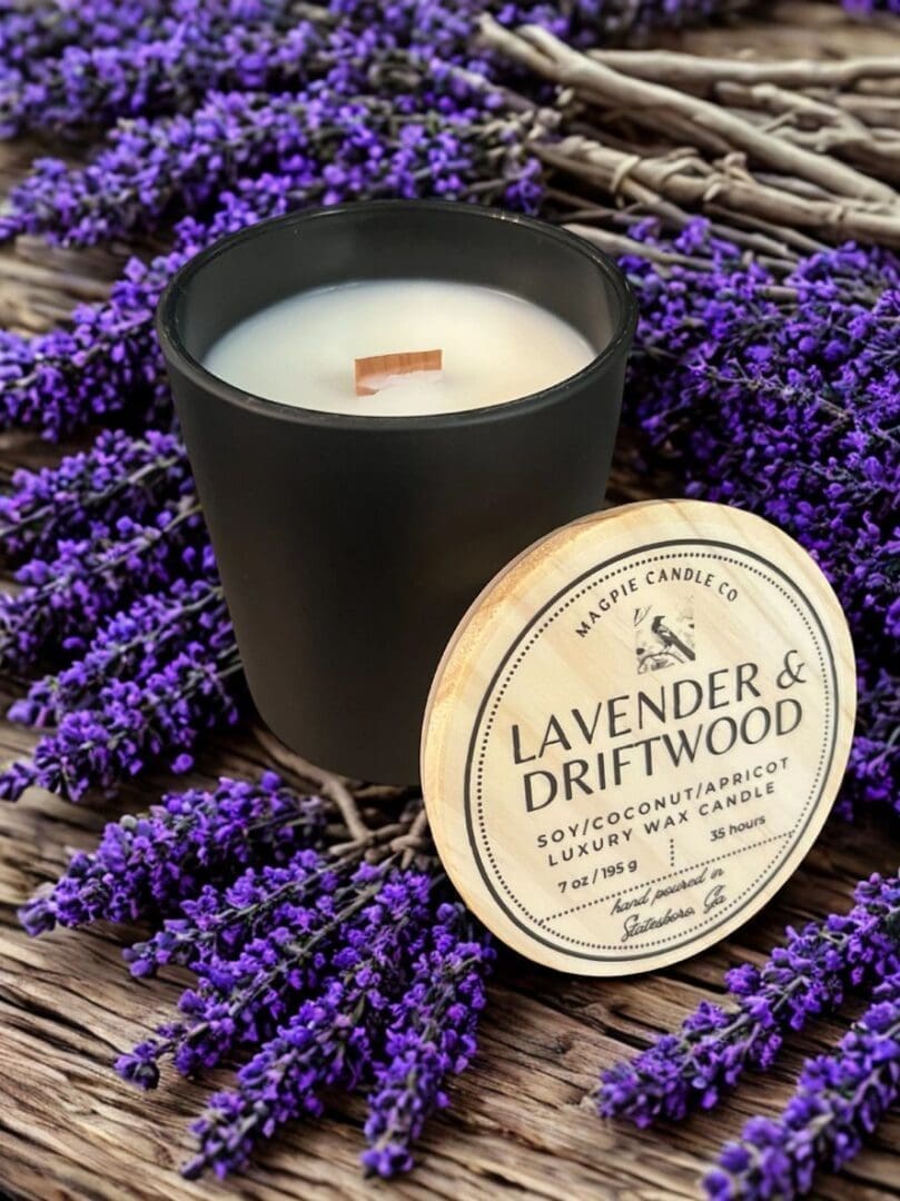 Black candle on lavender with lid nearby.
